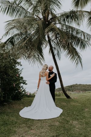 Couple shares intimate moment under swaying palm tree at tropical wedding venue.