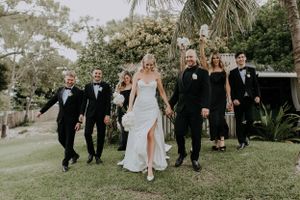 Wedding party walks together on manicured lawn with tropical landscaping.