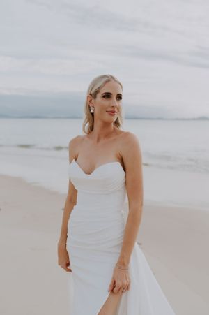 Elegant beach wedding portrait featuring a bride in a strapless white gown against a coastal backdrop.