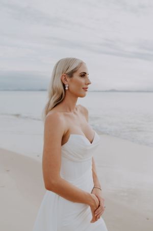 A bride poses in a fitted white wedding dress on a peaceful beach during sunset.