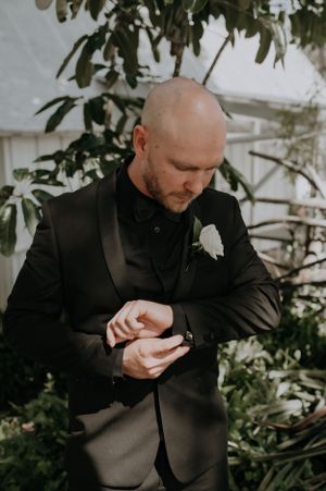 Groom in black tuxedo checking his watch while wearing a white boutonniere.