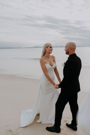 A couple shares an intimate moment on a sandy beach during their wedding photoshoot.
