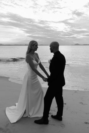 Black and white beach wedding photo capturing a tender moment between newlyweds at sunset.
