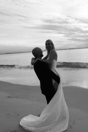 A black and white photo of a couple dancing intimately on a beach with waves in the background.