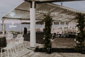 An elegant outdoor wedding reception venue with white chairs and string lights under a covered pavilion.