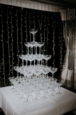 A tiered champagne tower display with crystal glasses against a backdrop of twinkling fairy lights.