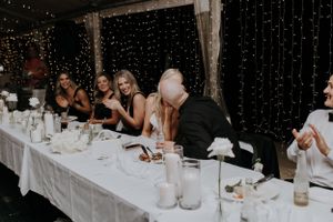 Wedding guests enjoying dinner at a long table decorated with candles and string light backdrop.
