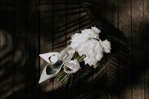 White roses and wedding rings arranged artistically on dark wooden surface with dramatic shadows.