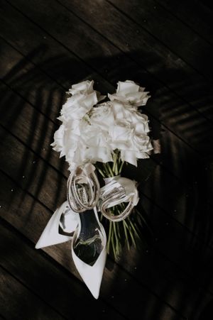 Wedding bouquet of white flowers with rings tied with white ribbon on dark wooden floor.