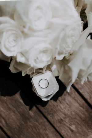 Wedding ring nestled among white roses on a rustic wooden surface.