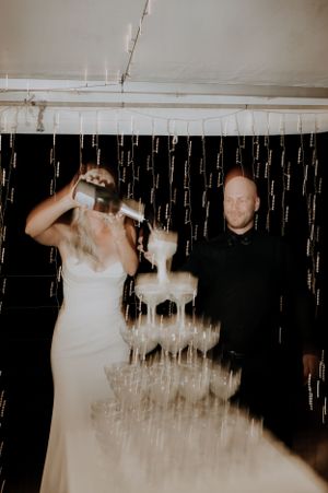 Wedding couple pouring champagne into a multi-tiered glass tower during their reception.