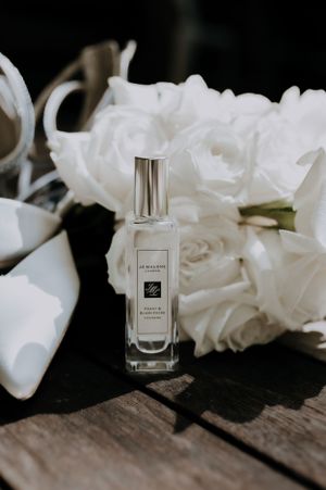 Glass perfume bottle displayed with white roses on wooden background.