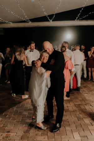 A tender slow dance moment under string lights on a brick patio at a wedding reception.
