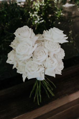 Elegant bouquet of white roses tied together with stems on dark surface.