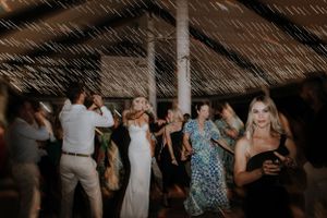 Wedding reception guests dancing and celebrating under string lights in a covered venue.