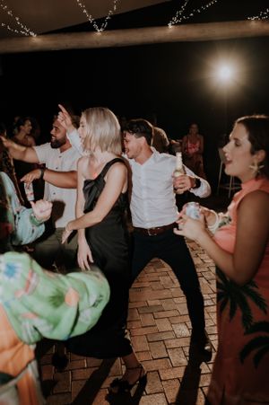 Wedding guests dancing energetically on a brick floor under twinkling reception lights.