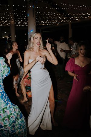 Guests dancing and celebrating at a wedding reception under twinkling string lights.