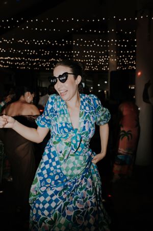 Woman in blue floral dress dancing under string lights at an evening party.