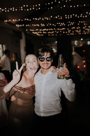 Two party guests posing with drinks and peace signs under string lights at night.