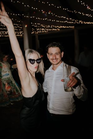 Couple in black and white attire dancing and celebrating under twinkling lights.