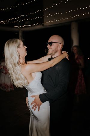 Couple dancing closely beneath string lights at an evening celebration.