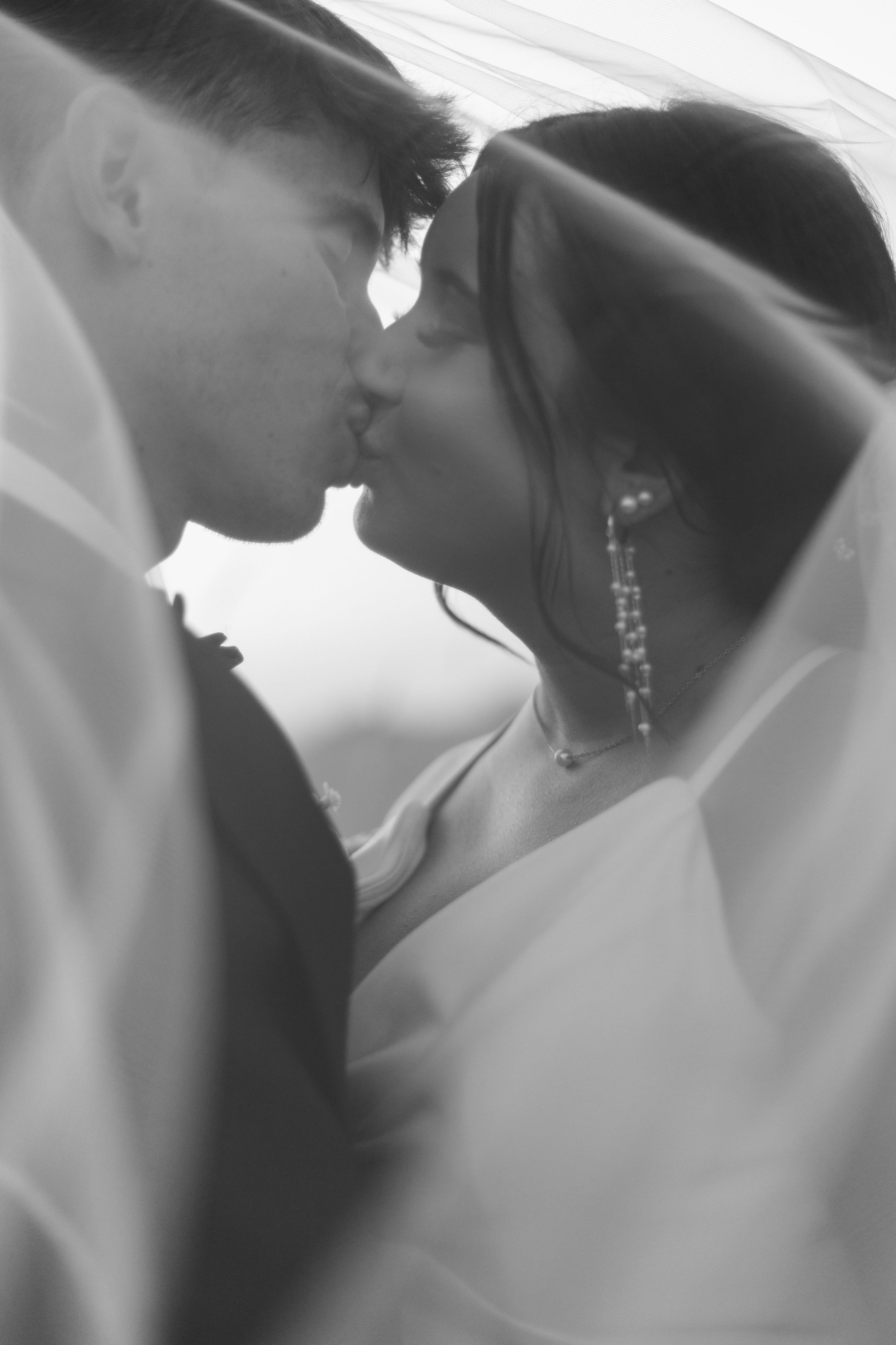 Black and white intimate portrait of newlyweds under bridal veil.