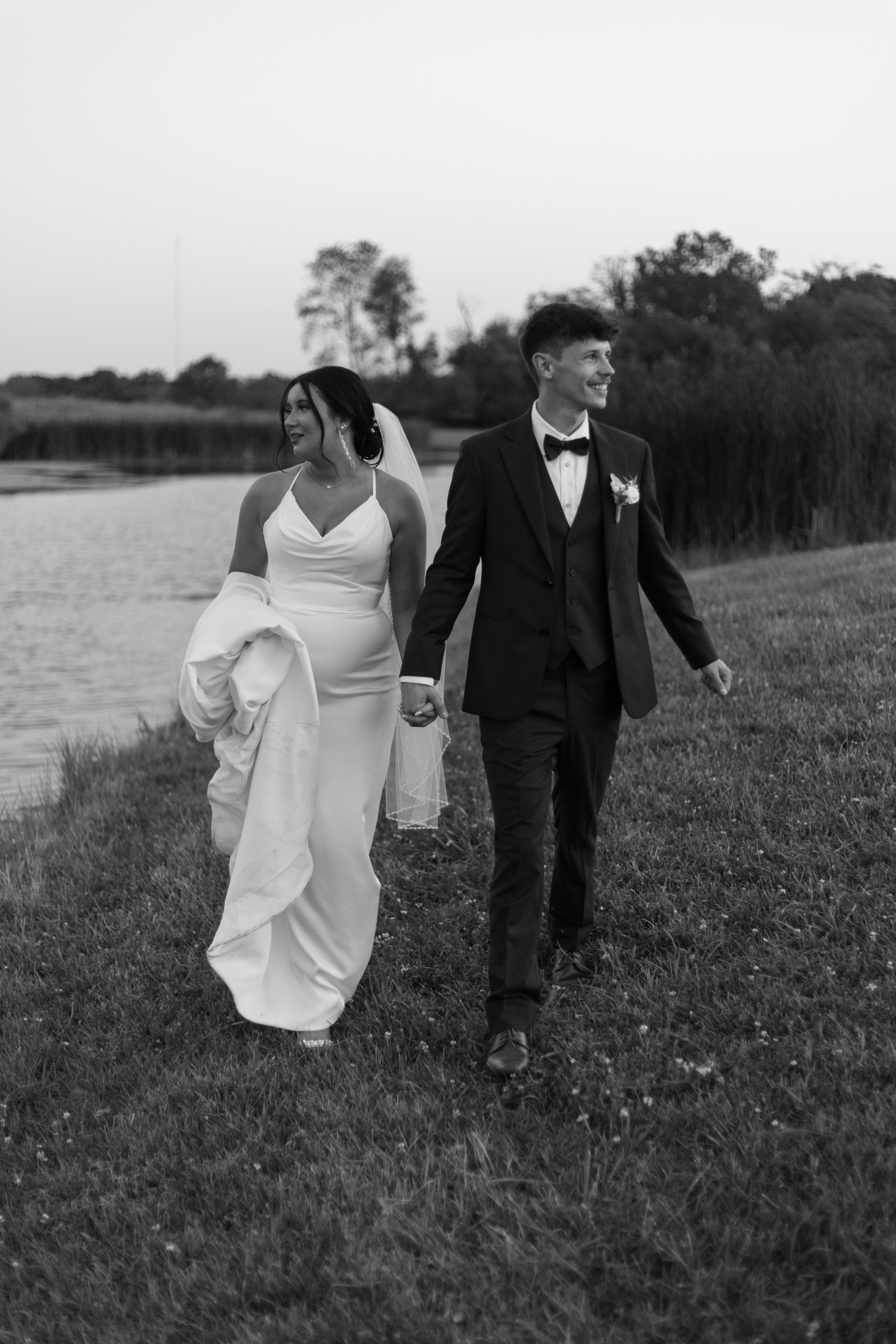 Bride and groom walking together by waterfront in black and white photo.