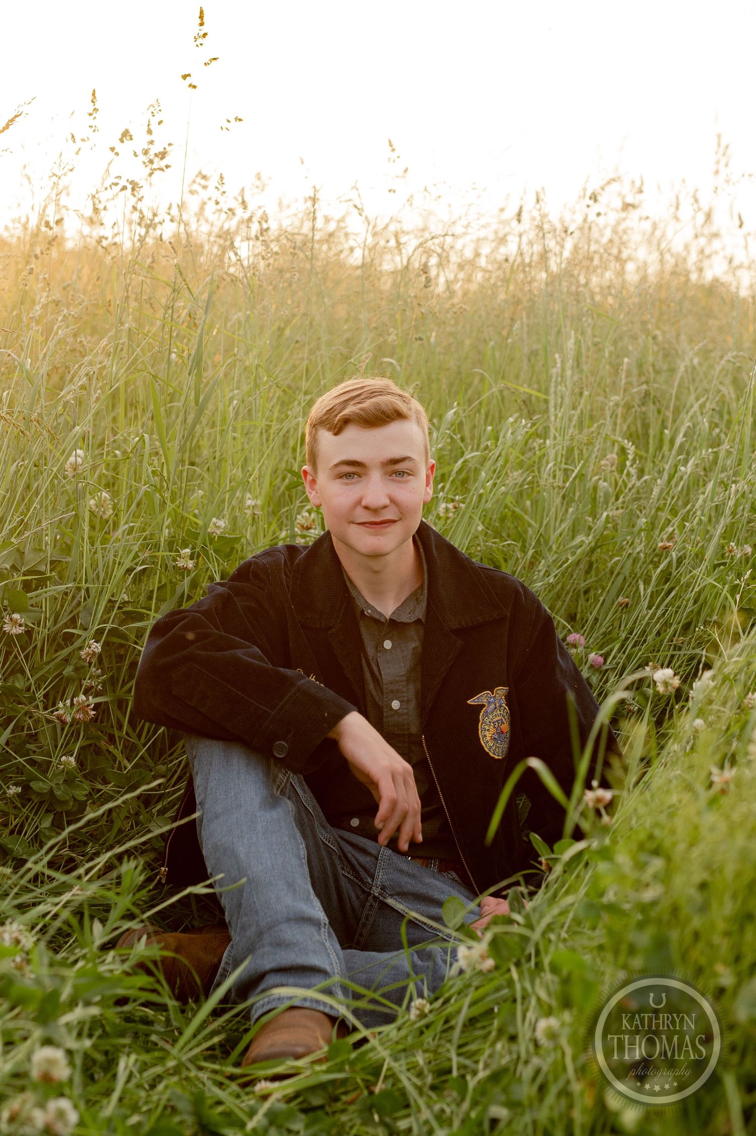 Casual senior photo of FFA student sitting in tall grass during golden hour.