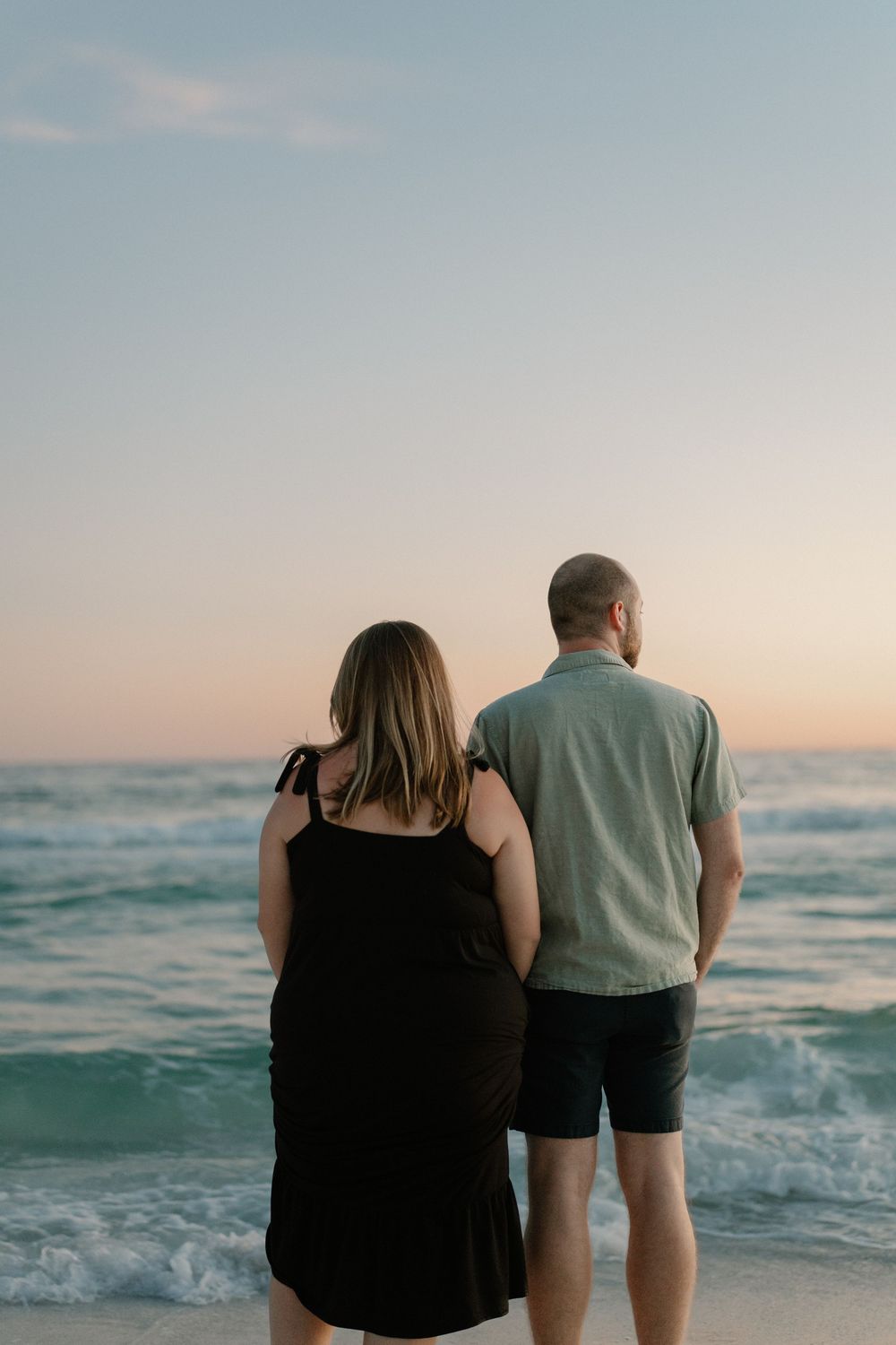 A couple stands together watching ocean waves at sunset on a peaceful beach.