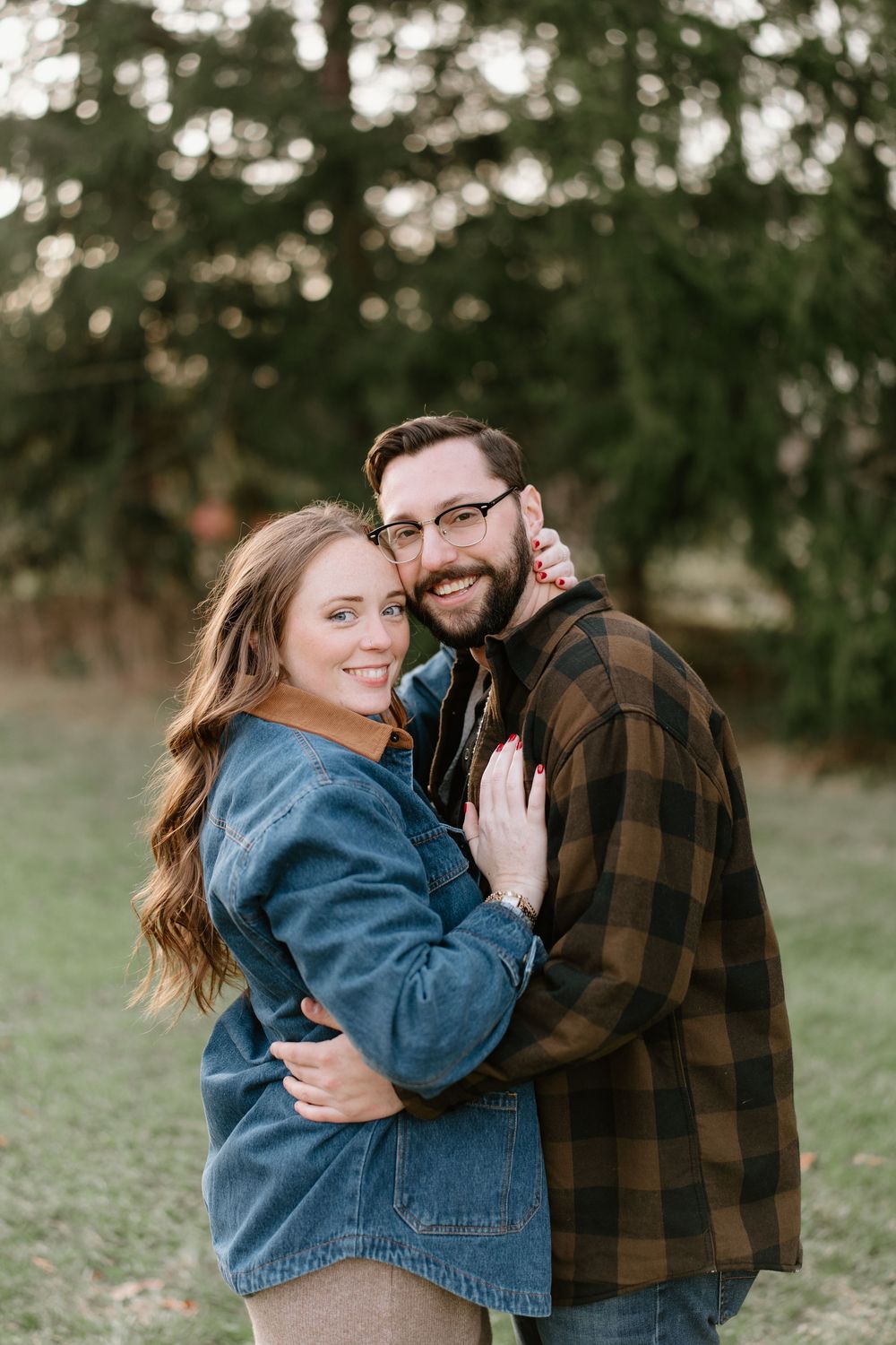 A couple embraces outdoors wearing casual denim and plaid while sharing a joyful moment in a natural setting.