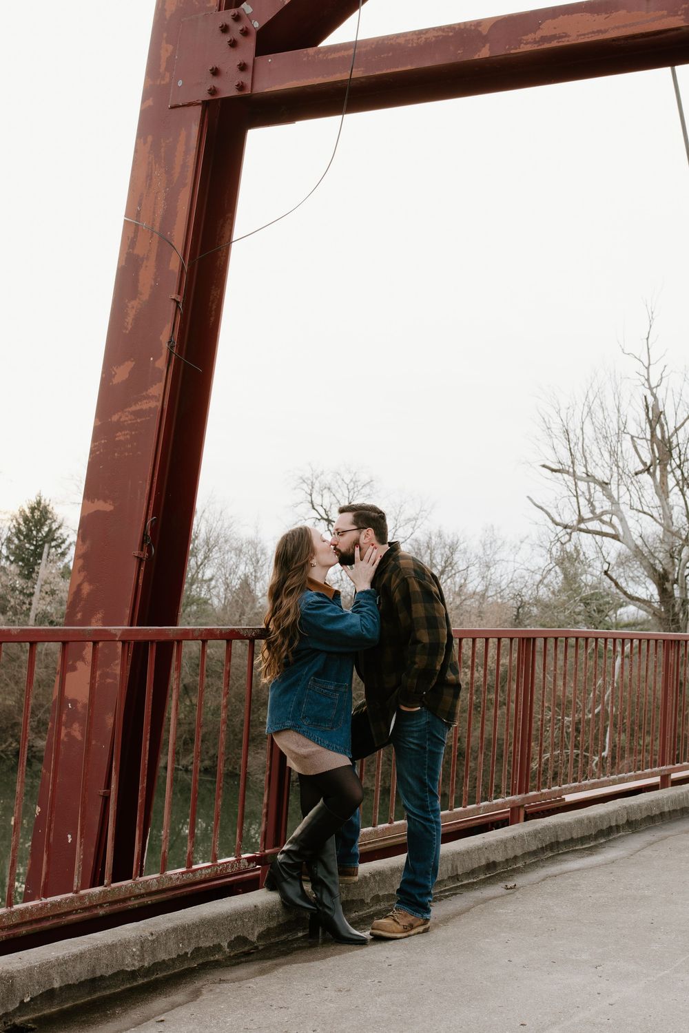 A romantic couple sharing intimate moments on a rustic red bridge in a natural setting.