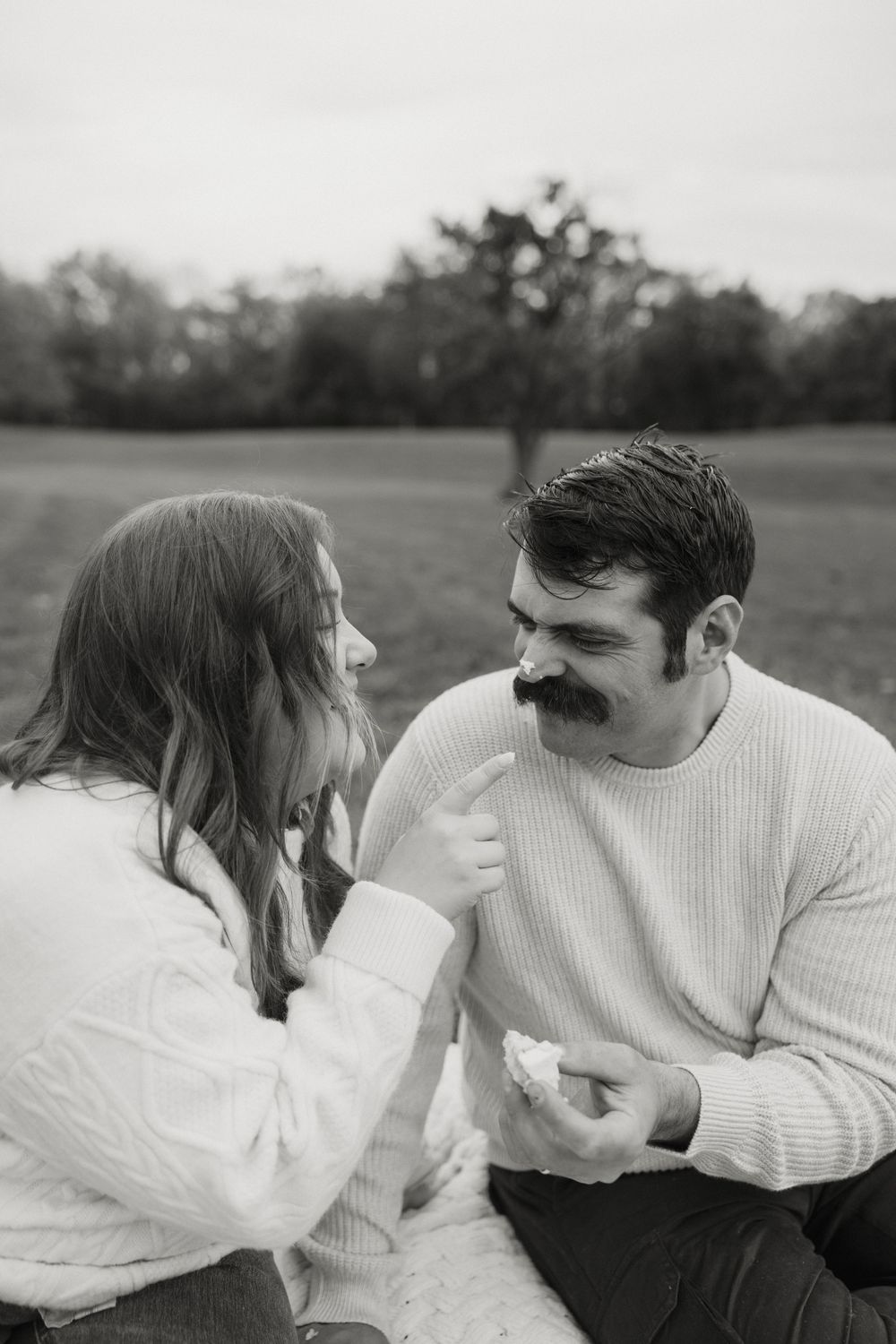 A couple shares an intimate black and white moment during their picnic on a blanket outdoors.