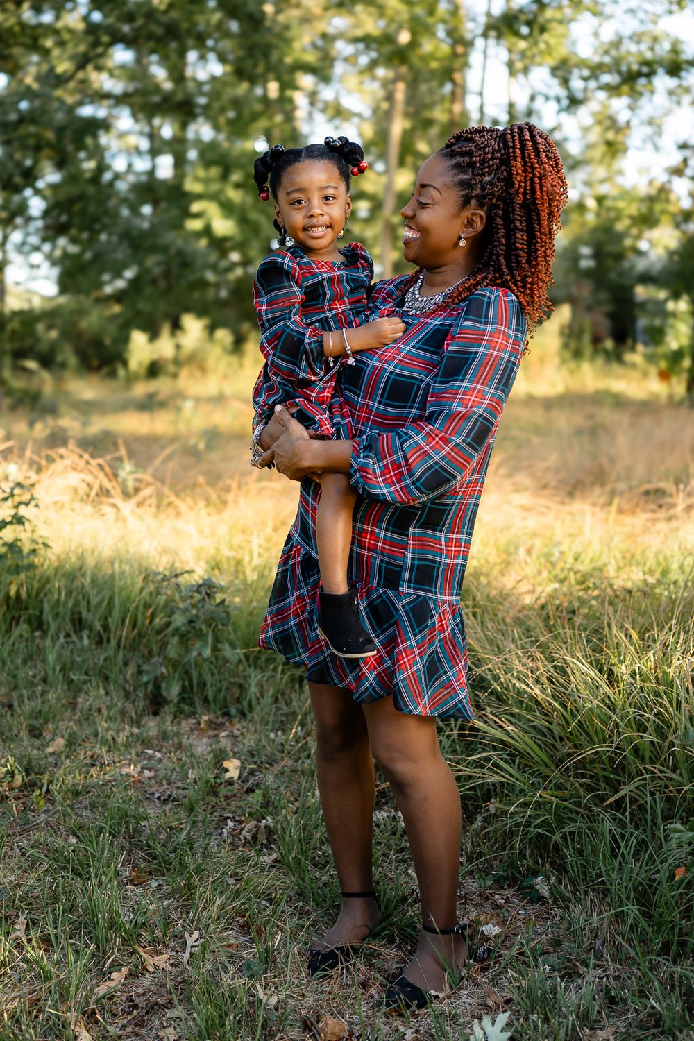 Mother and child share joyful moment outdoors wearing matching plaid outfits.
