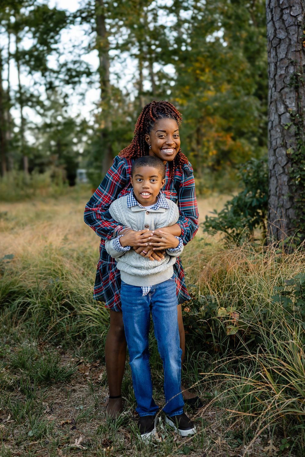 Playful embrace between parent and child outdoors with autumn trees in background.