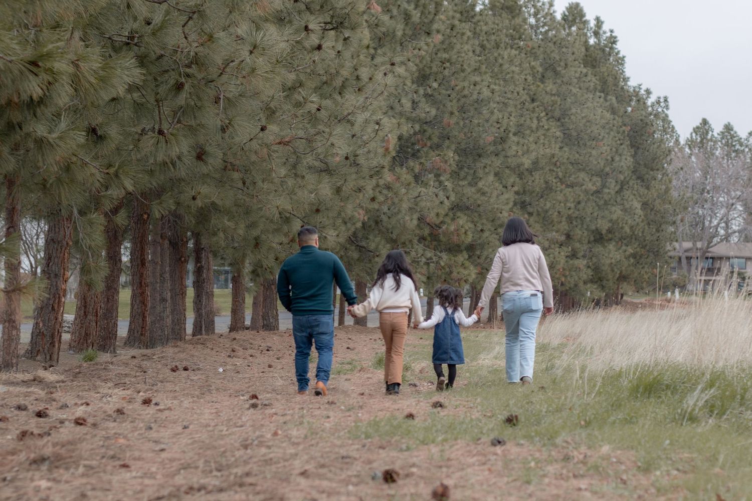 Family of four walking hand in hand down a wooded path during fall session in Tri-Cities WA
