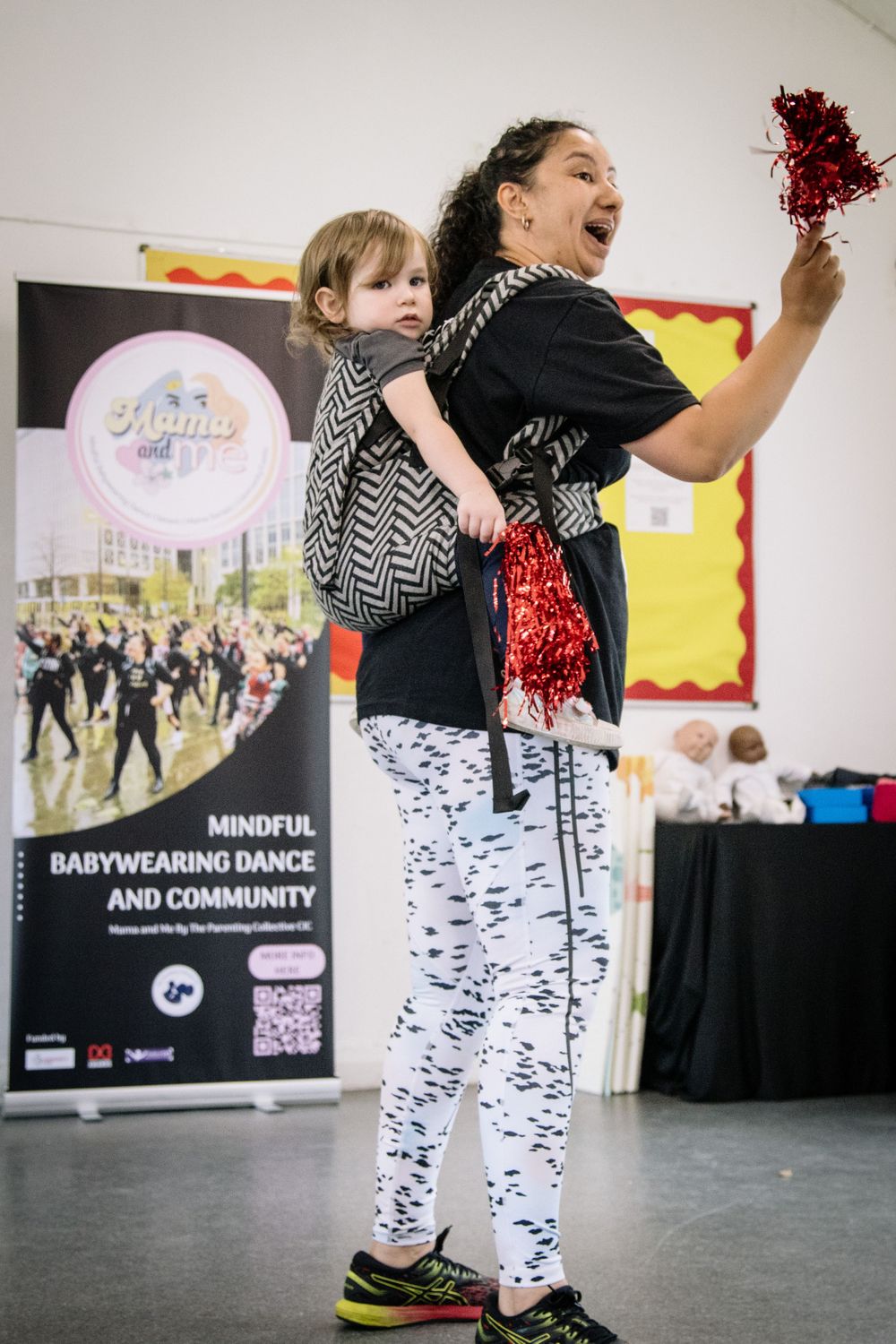 Enthusiastic participant dancing with baby in carrier at community dance event.