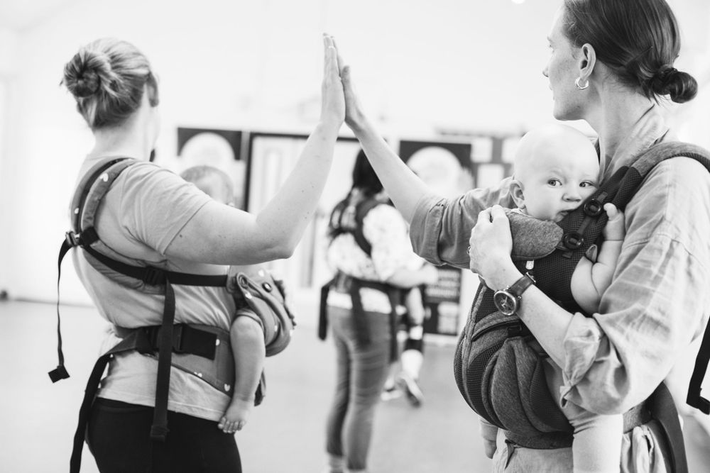 Parents and babies participating in a dance exercise class wearing baby carriers.