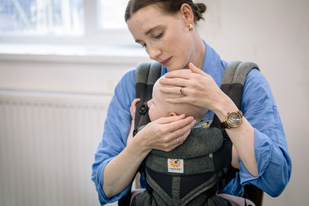 A parent wearing a blue shirt tenderly gazes at their baby in a baby sling.