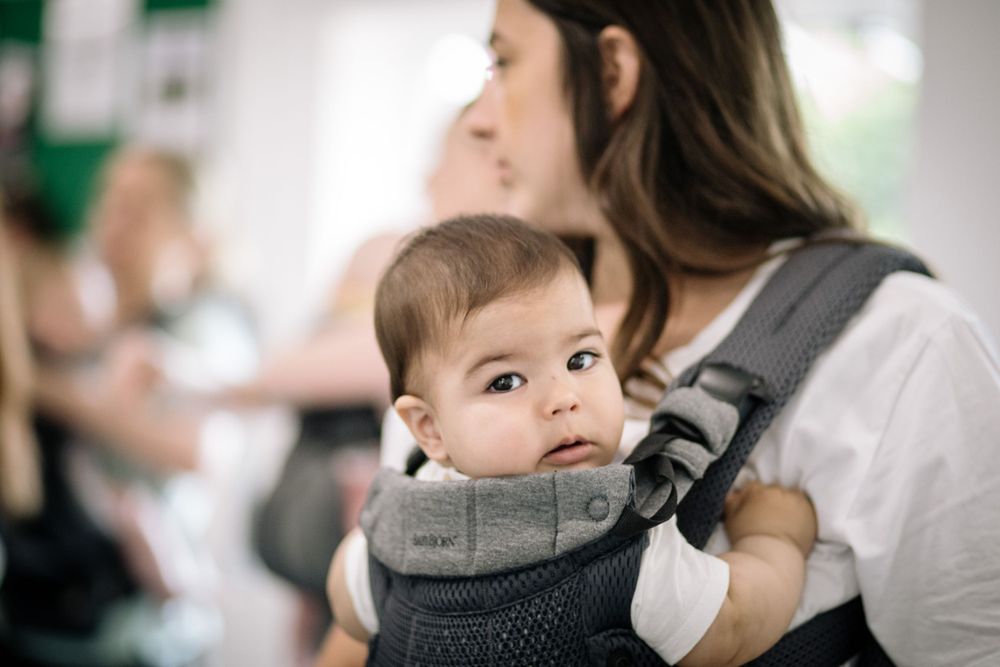 Baby in gray carrier looks on curiously during movement class.
