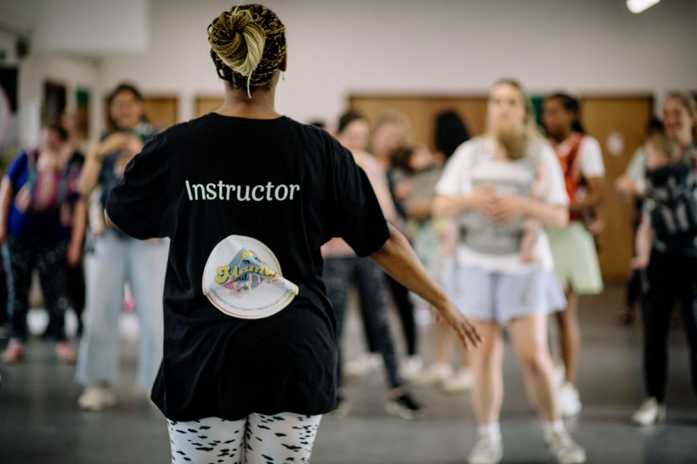 Dance instructor in black t-shirt leads class while demonstrating movements.