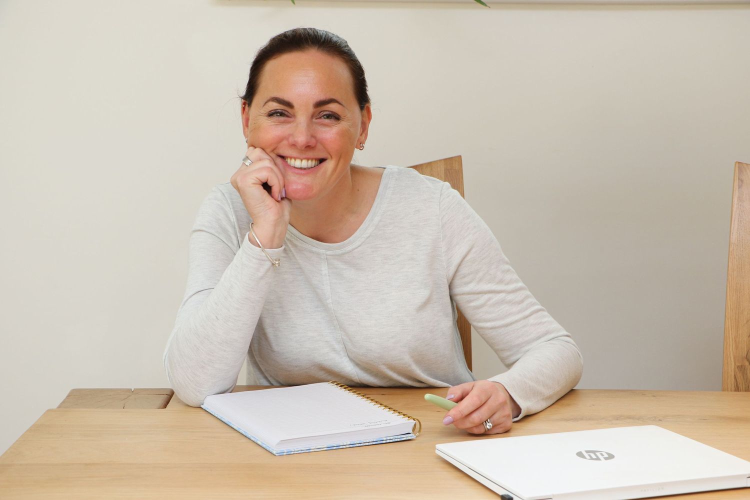 A person in light gray sweater smiling while working at desk with papers.
