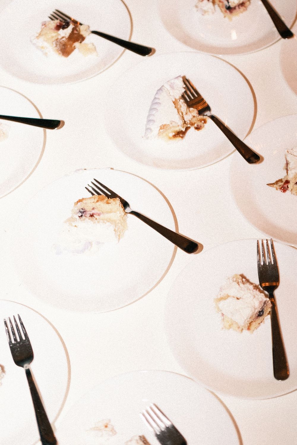 Overhead view of white plates with forks and partially eaten slices of wedding cake with frosting crumbs on a white tablecloth.