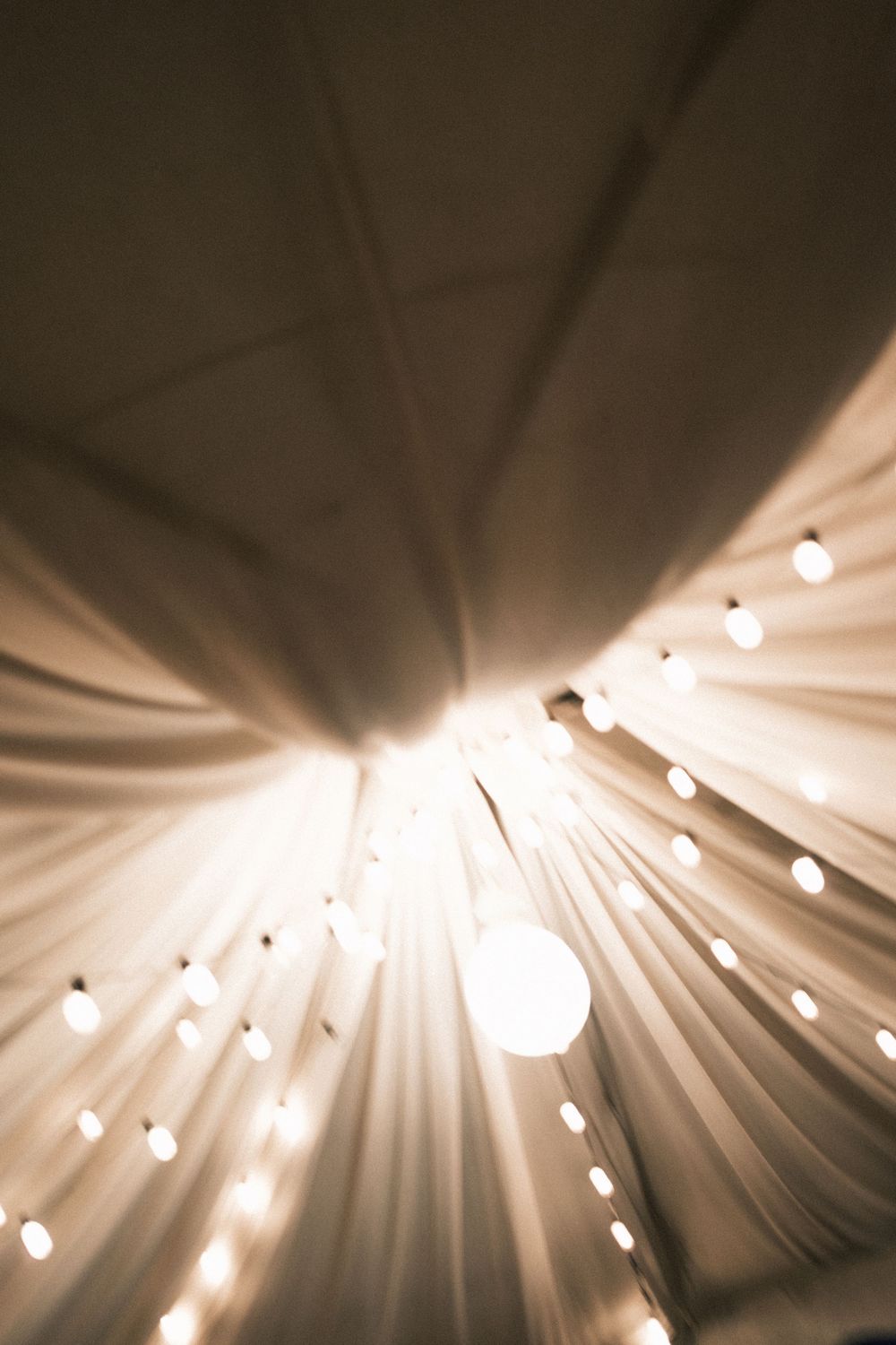 Draped white fabric canopy ceiling with glowing string lights and a large globe bulb creating a warm, romantic tent atmosphere.
