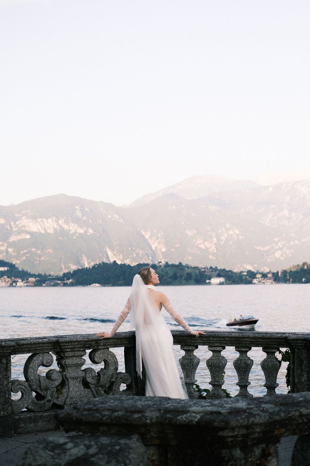 Bride in flowing gown overlooking Lake Como villa view.