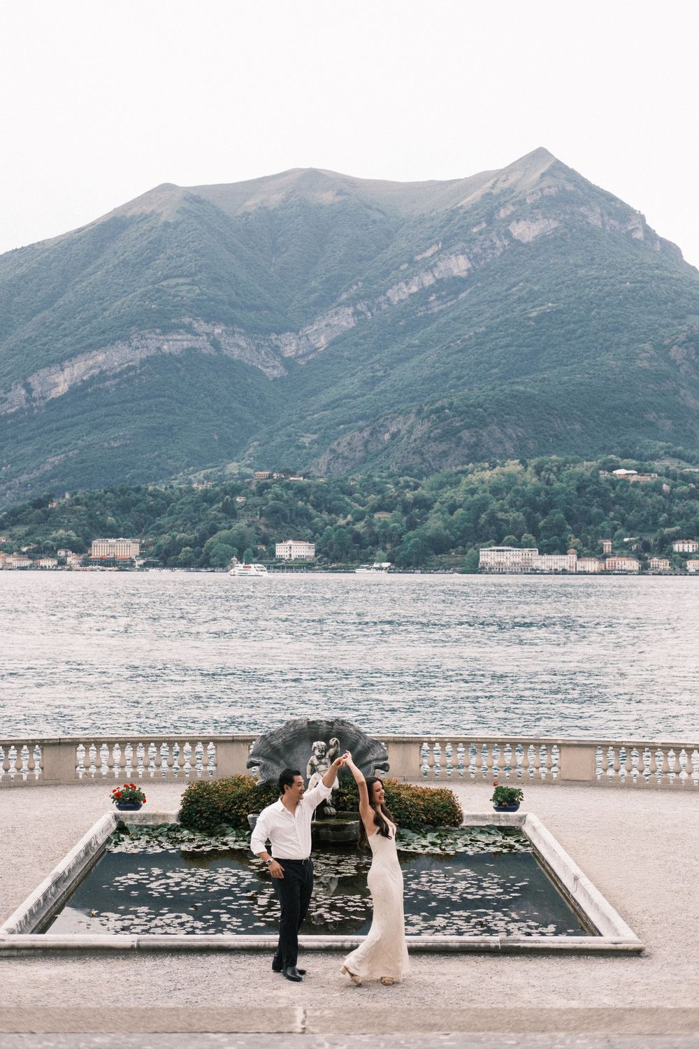 Couple dancing on a lakeside terrace with mountain backdrop at Lake Como, Italy, during a romantic wedding celebration.