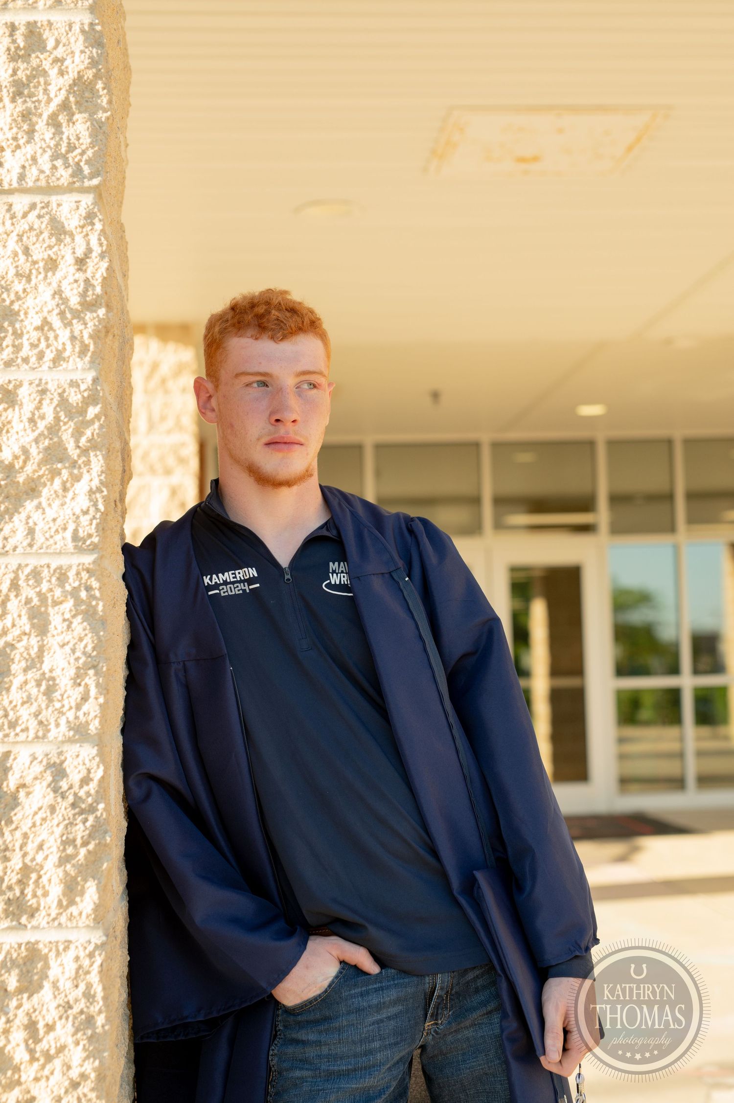 Graduate in navy jacket poses against textured stone wall entrance.