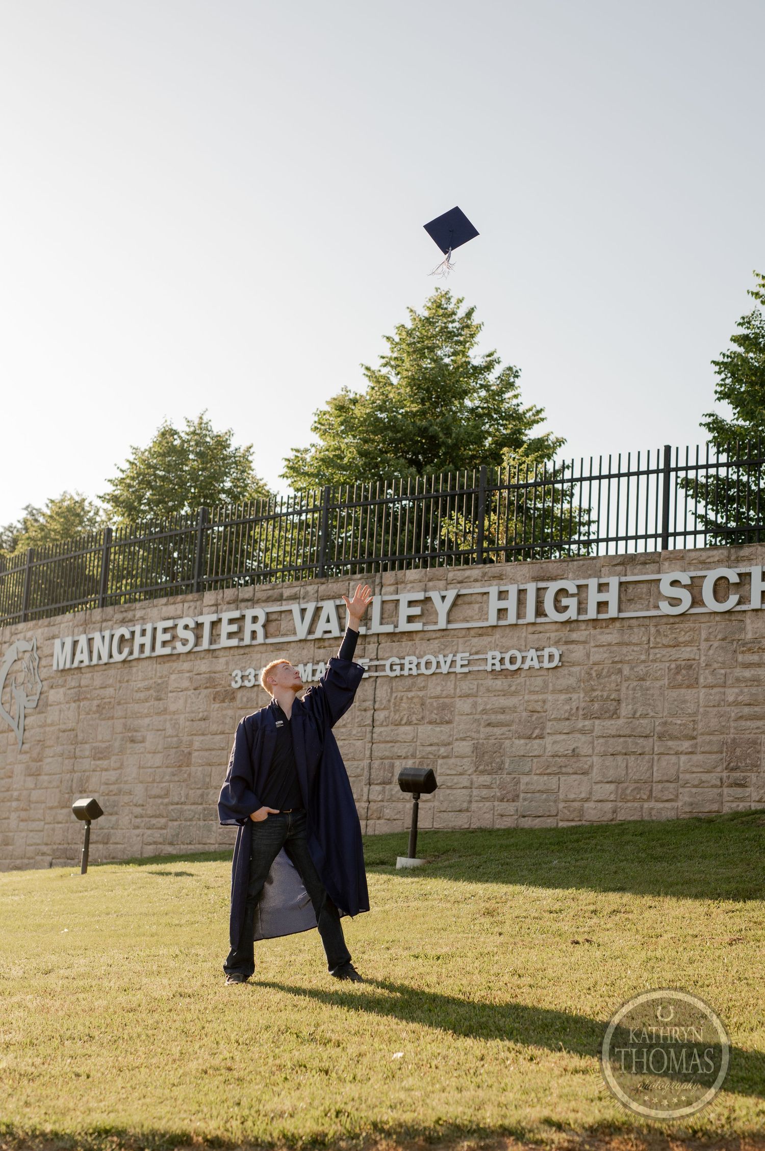 Graduate tosses graduation cap in the air at Manchester Valley High School entrance.