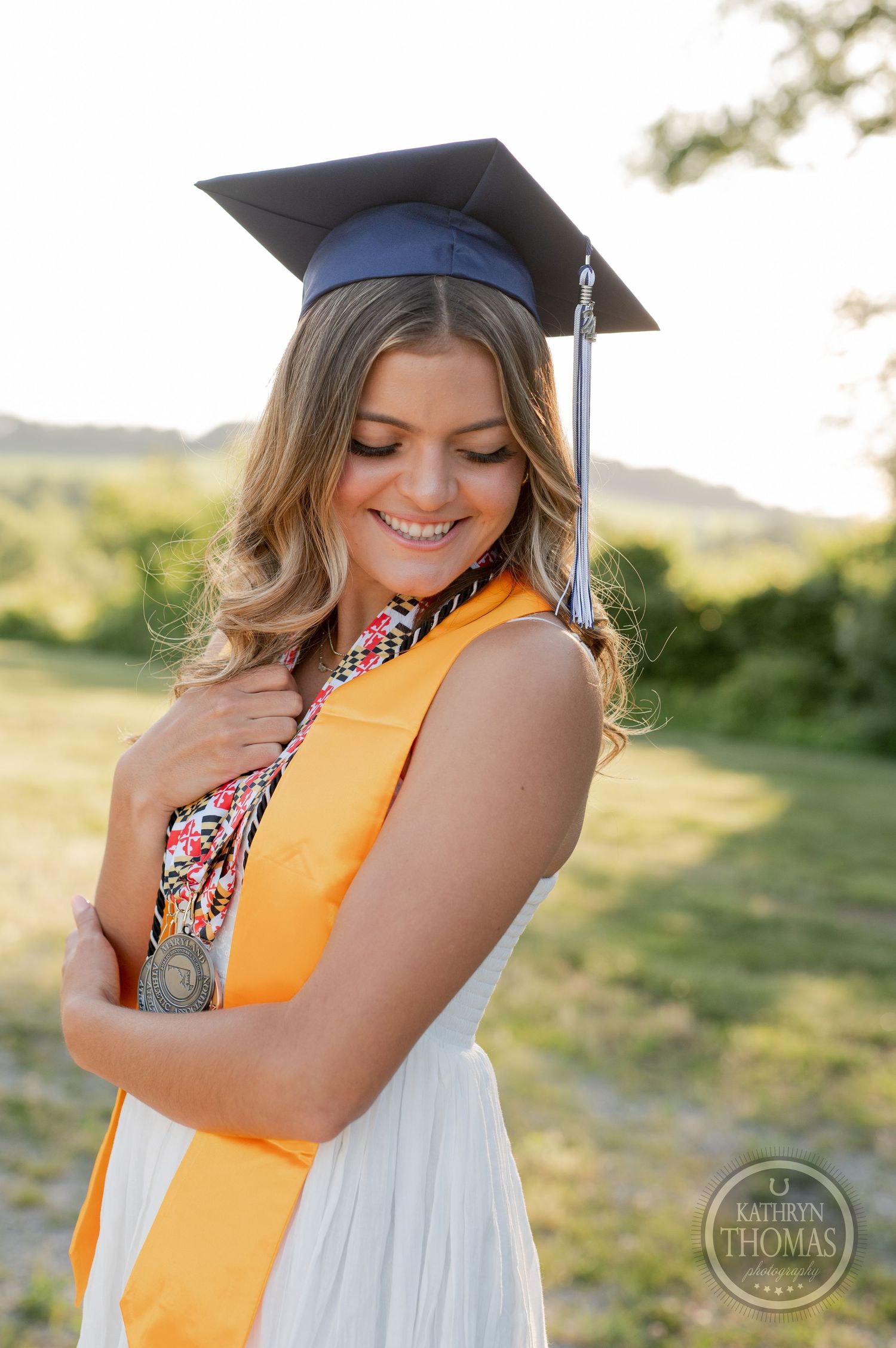 Graduate wearing navy cap with bright yellow stole poses during sunset graduation photos.