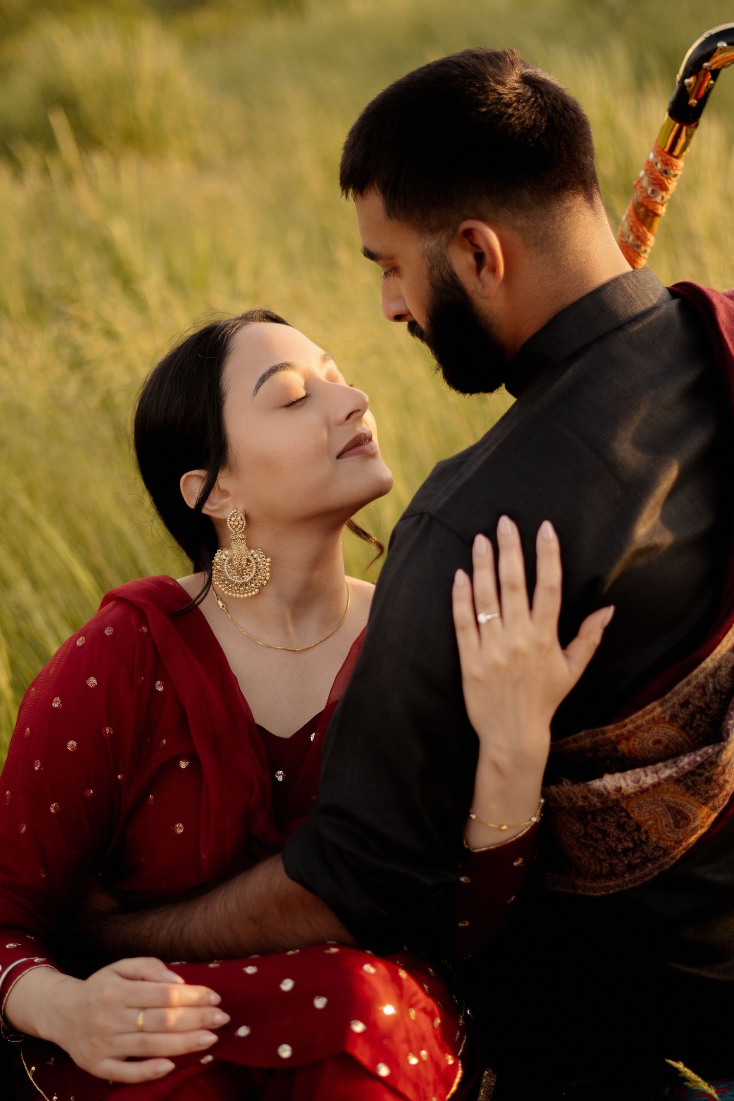 A romantic couple embraces in a field of tall grass, with her wearing red and him wearing black.