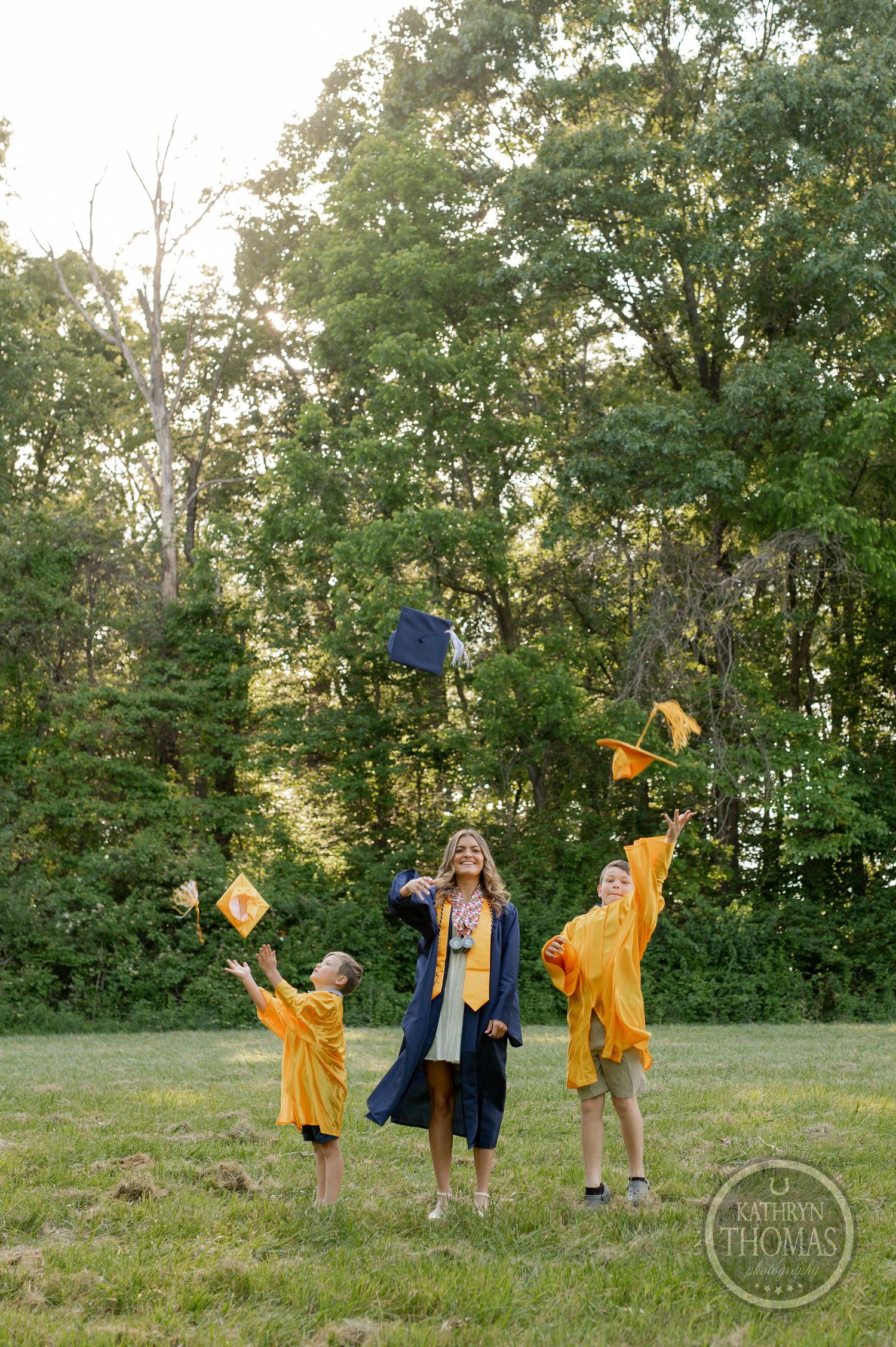 Graduates toss caps in celebration on grass field with trees in background.